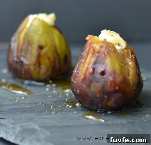 Two grilled figs stuffed with Brie cheese and drizzled with honey on a gray surface.