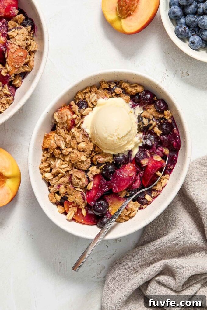 Peach blueberry crisp in a bowl with ice cream.