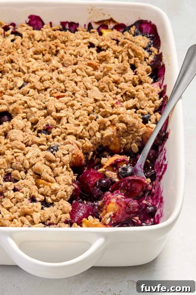 Peach and Blueberry Crisp Recipe with Oat Topping 6 Spoon digging into peach and blueberry crisp in baking dish.