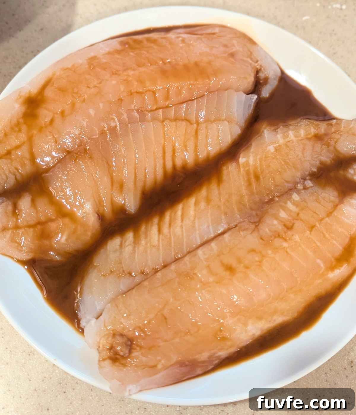 Tilapia fillets marinated in teriyaki sauce and placed on a white plate.