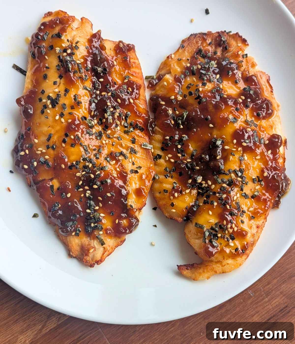 Teriyaki tilapia fillets garnished with furikake on a white plate.