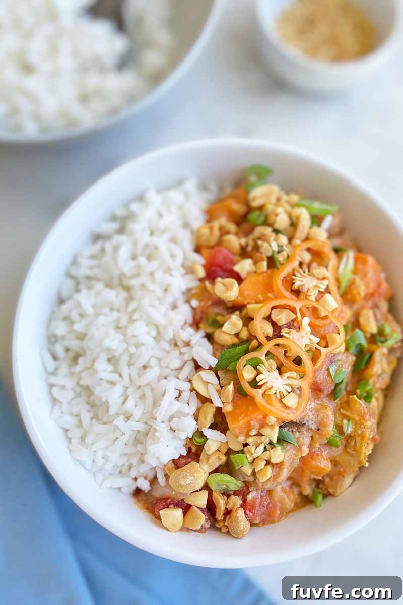 Vertical image of a white bowl with white rice and a thick poultry and vegetable mixture next to a blue napkin.