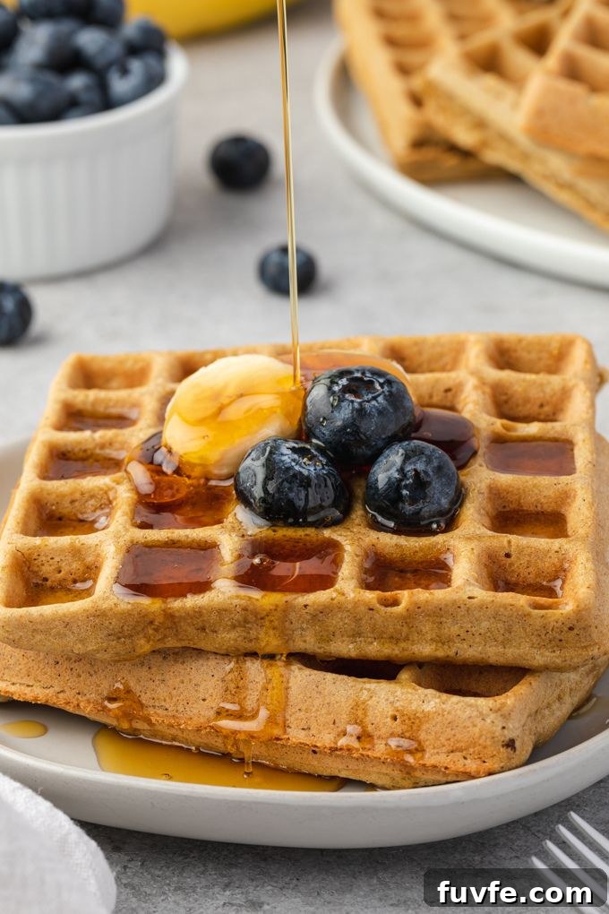 Gluten-free oat waffles with maple syrup pouring over the top