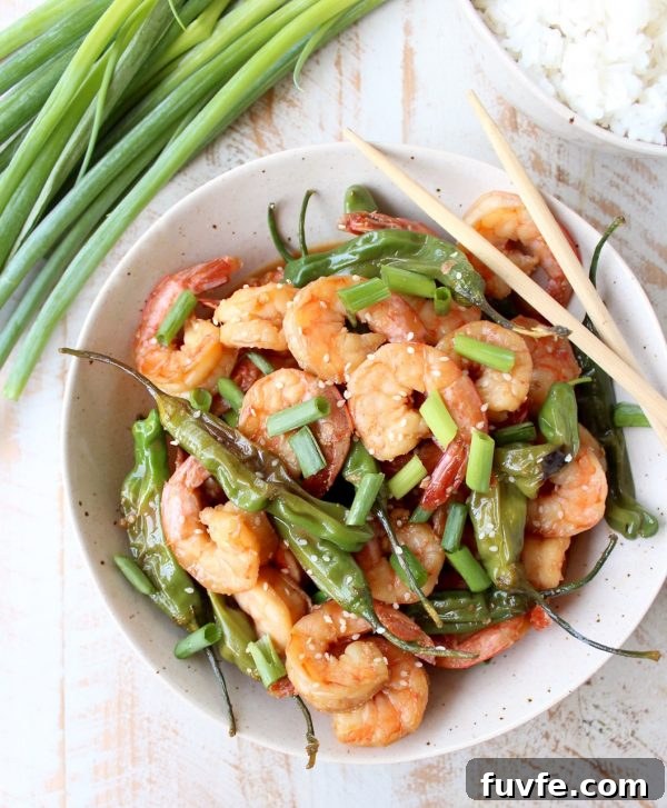 Overhead view of shishito shrimp stir fry in a white bowl with chopsticks.