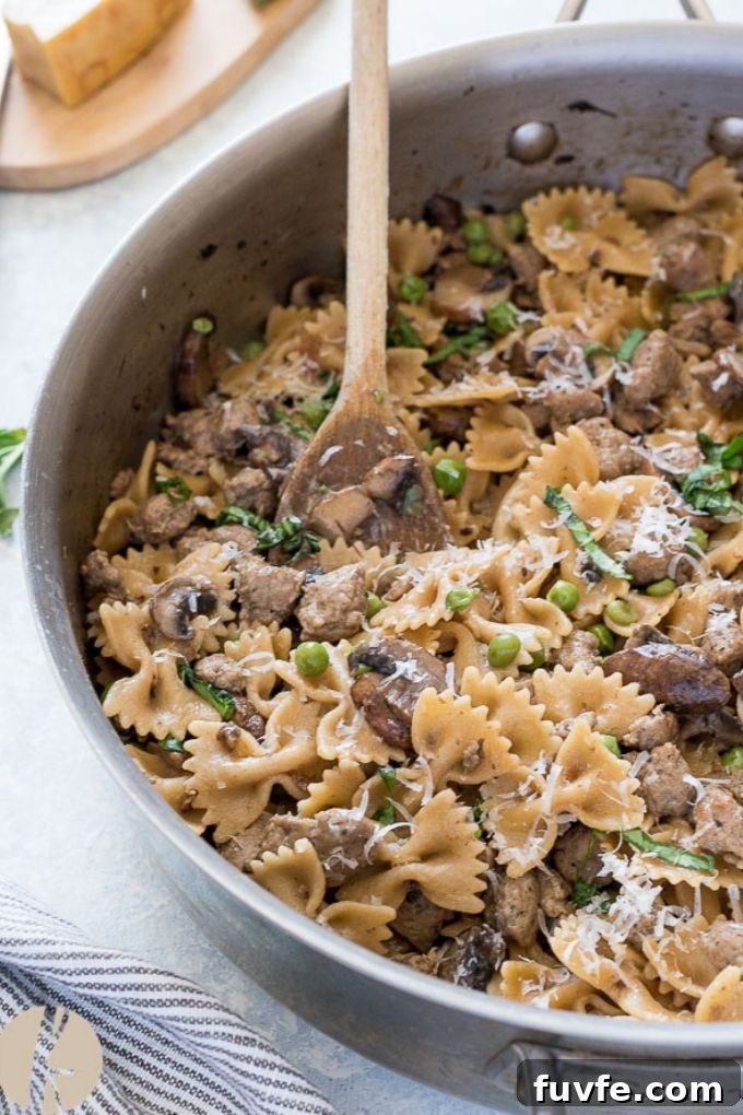 Wooden spoon scooping bow tie and sausage pasta in skillet