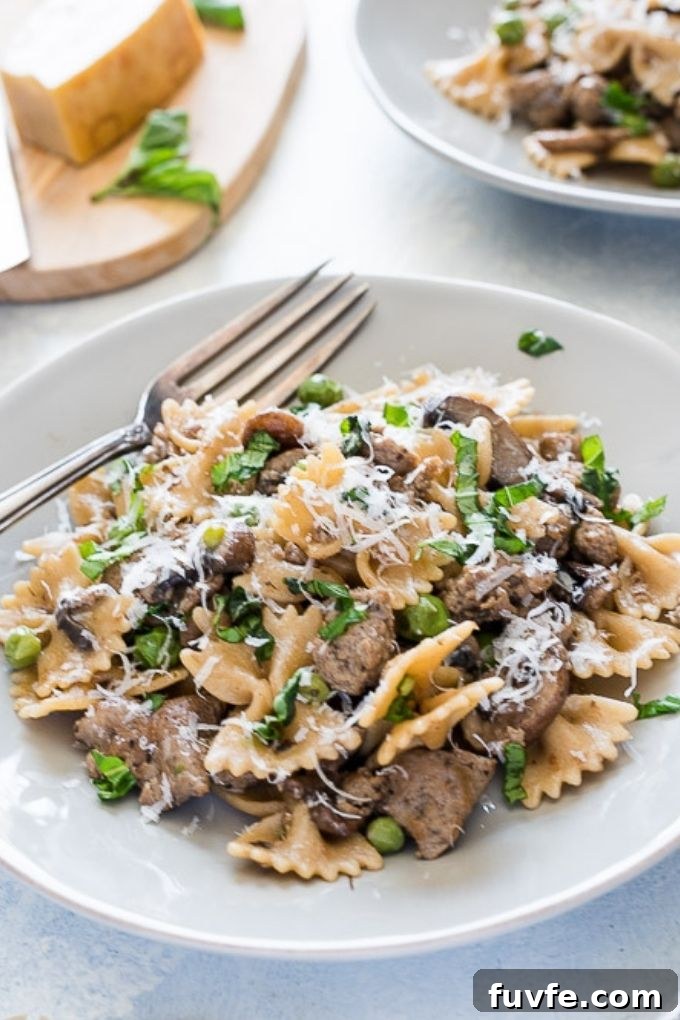 Plate of sausage bow tie pasta topped with parmesan cheese and basil