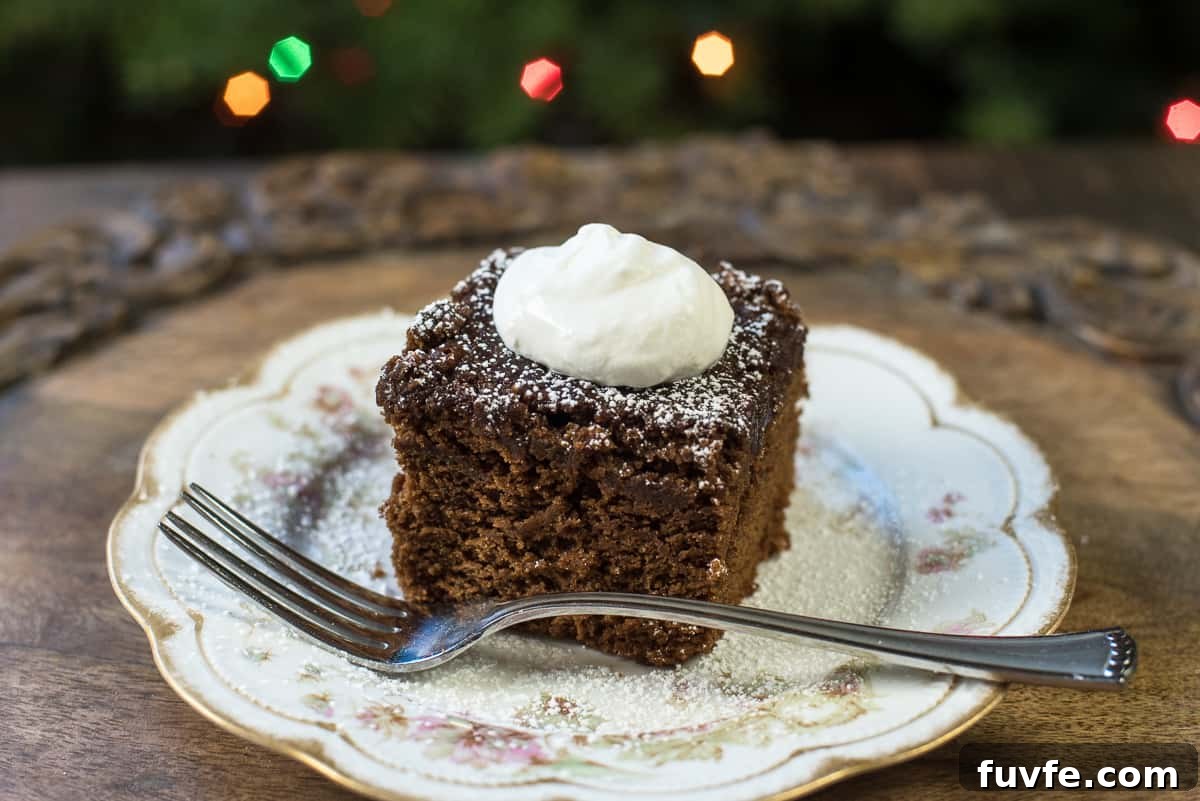 Warm Gingerbread Cake Recipe with Spiced Molasses Glaze 5 A slice of gingerbread topped with powdered sugar and whipped cream on a pretty china plate with a fork.