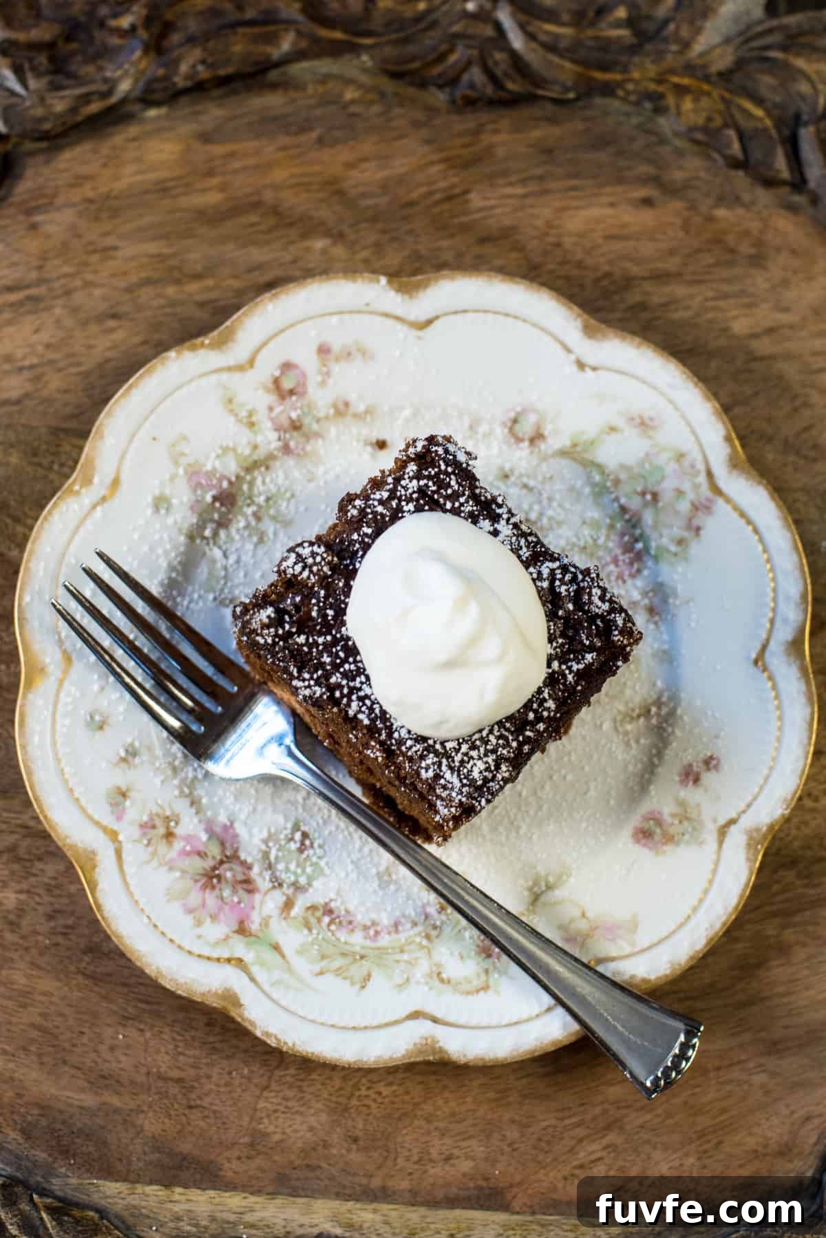 Warm Gingerbread Cake Recipe with Spiced Molasses Glaze 7 A top down shot of a slice of gingerbread topped with whipped cream on a pretty china plate with a fork.