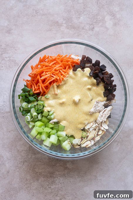 Creamy curry dressing in bowl with curry chicken salad ingredients before mixing.