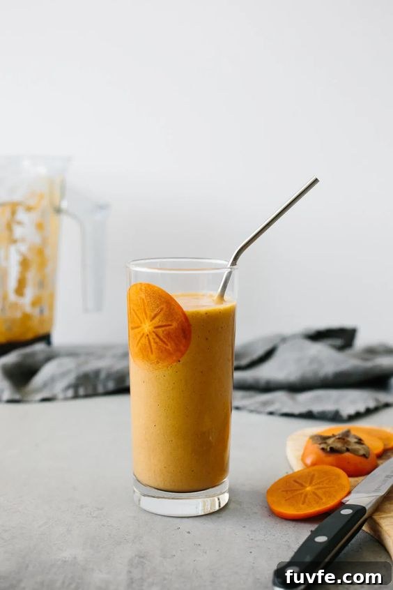 A persimmon smoothie in a glass with a straw.