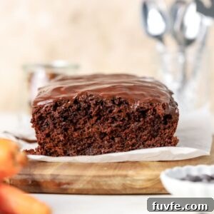 A chocolate loaf cake topped with chocolate glaze next to some carrots.