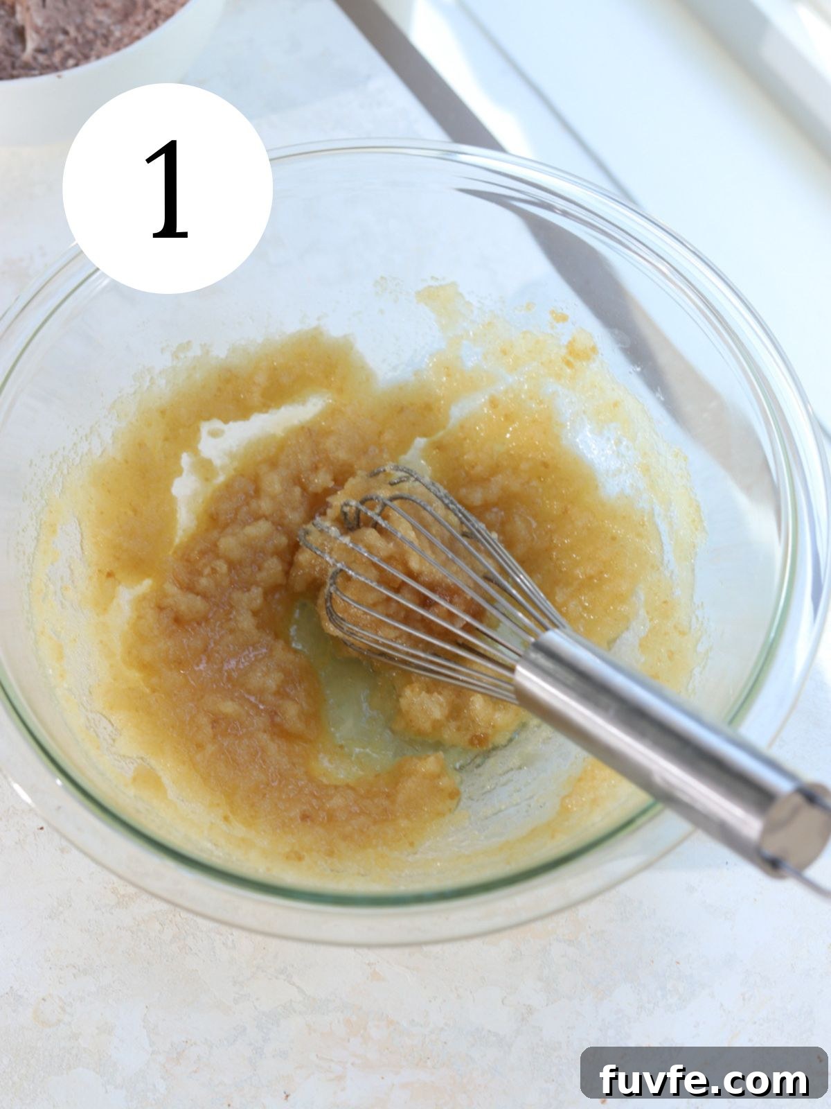 A glass mixing bowl with butter and sugar whisked together.
