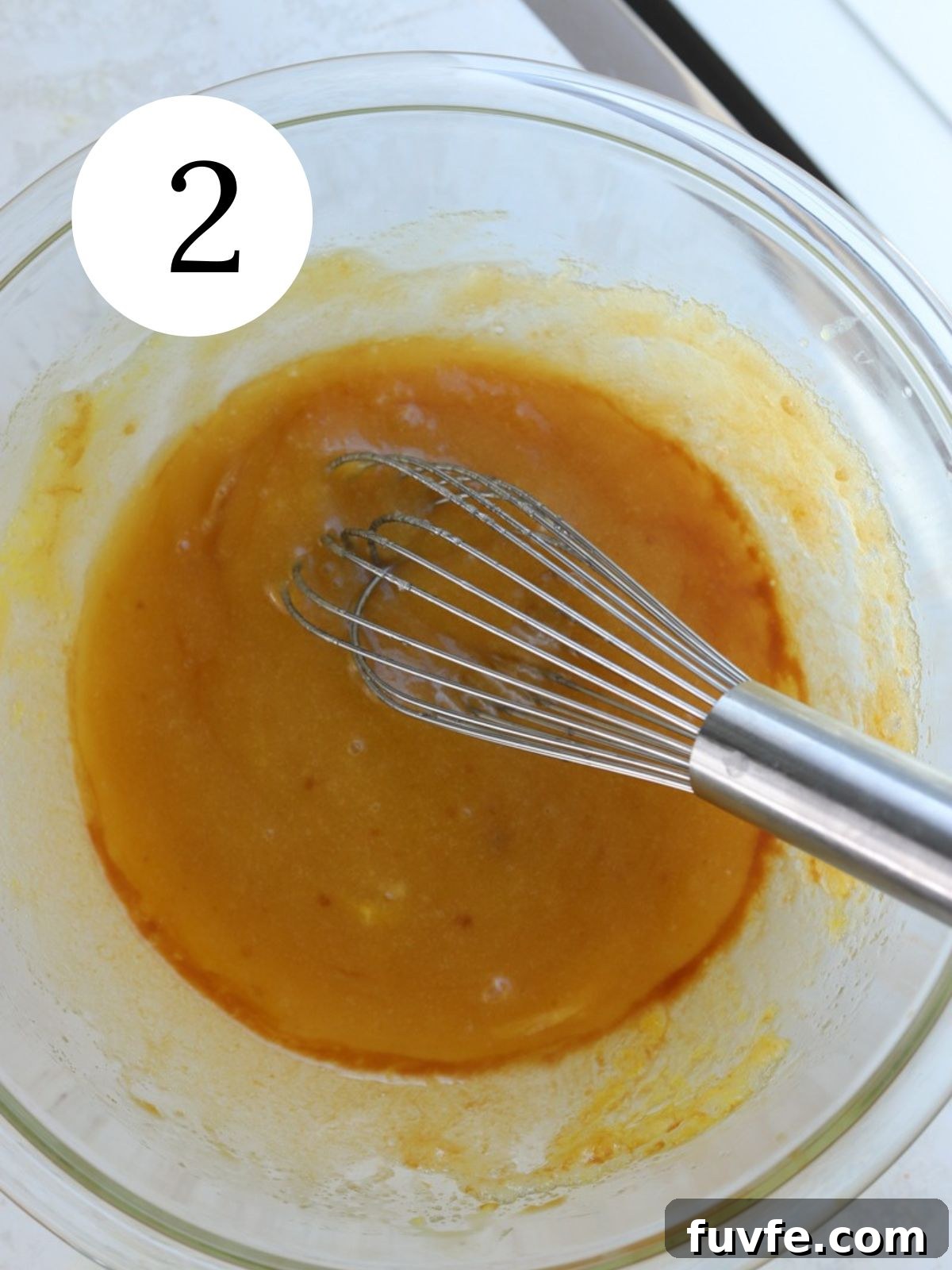 A glass mixing bowl with a whisk and a mixture in it.