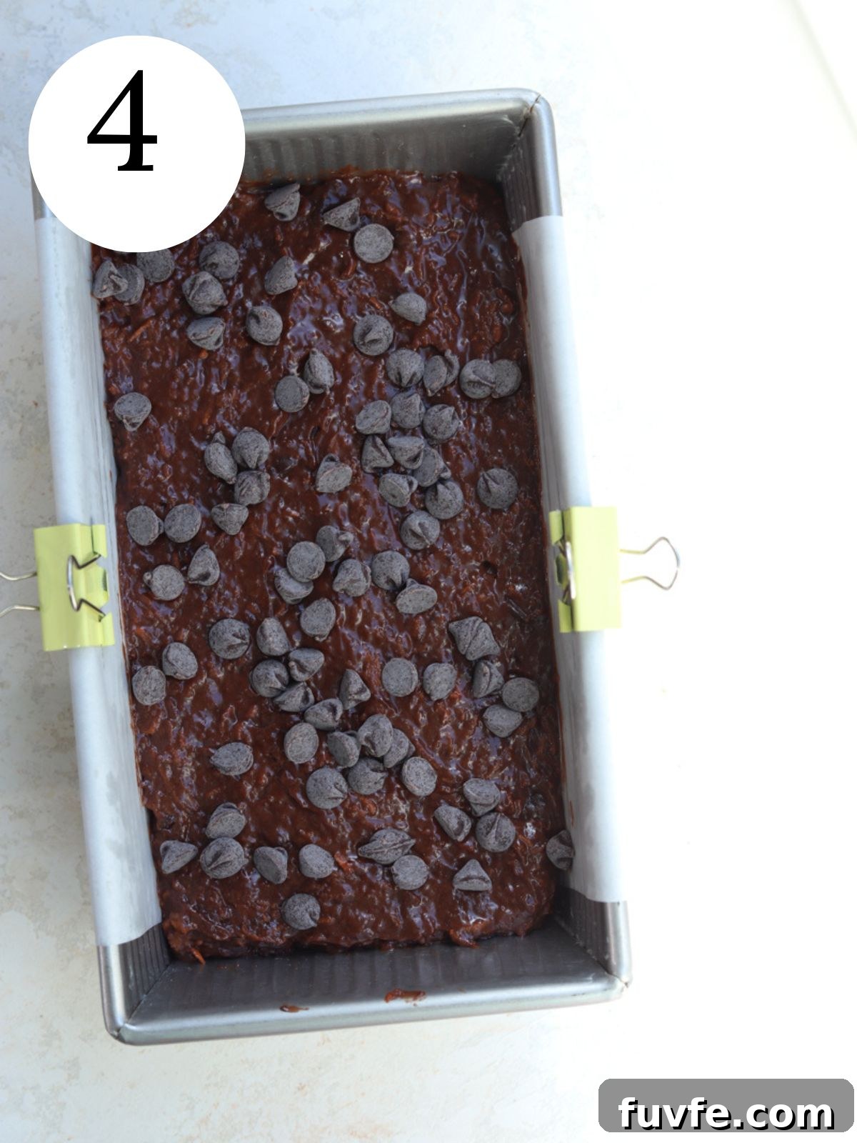 A chocolate loaf cake in a loaf pan with chocolate chips on top.