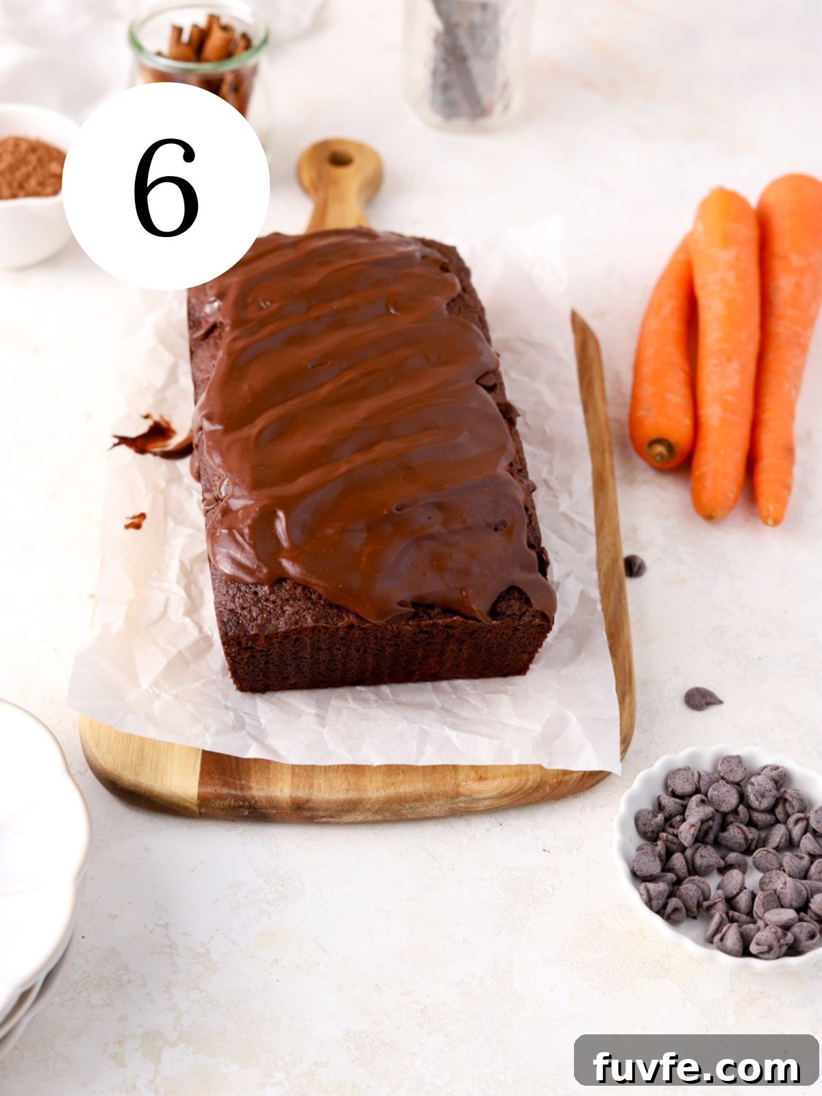 A chocolate loaf cake with chocolate glaze next to some carrots and chocolate chips.
