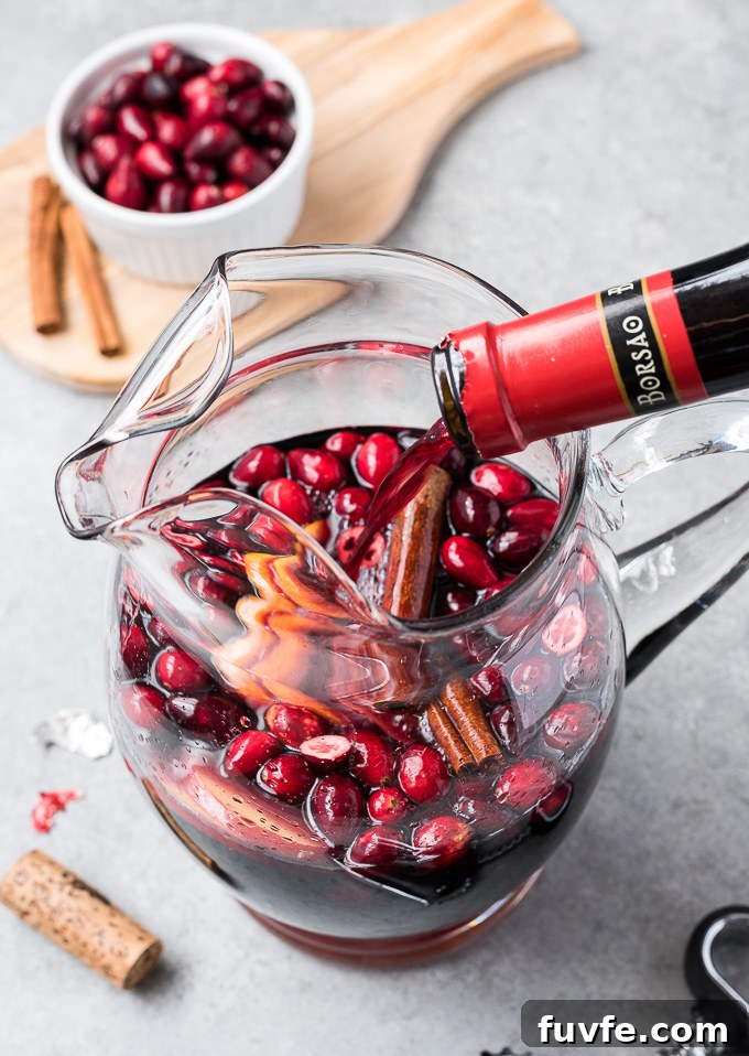 Cranberry Sangria Recipe for Holiday Parties 3 Cranberry sangria in a pitcher with red wine pouring in