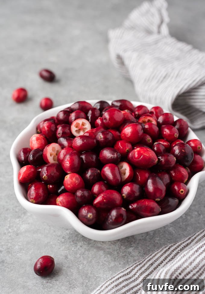 Fresh cranberries in a white bowl with some cut in half