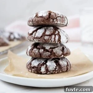 15 Irresistible Chocolate Sourdough Recipes to Try Today 26 A stack of 4 sourdough chocolate crinkle cookies sitting on a small white plate lined with parchment paper.