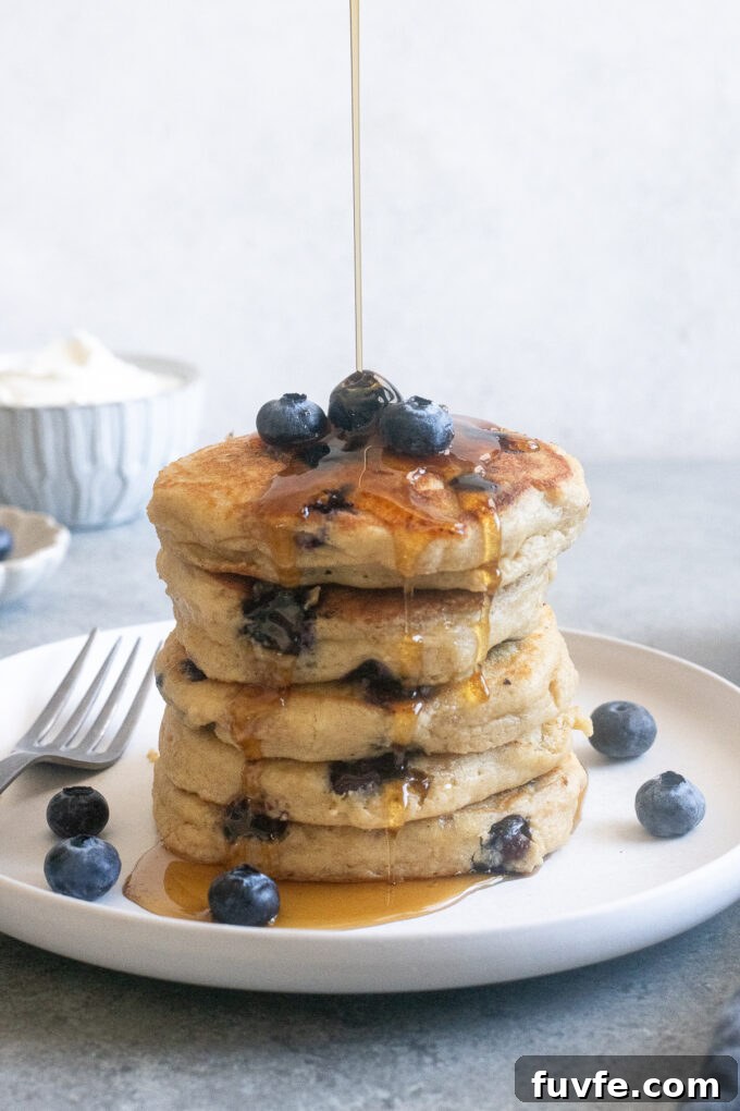 Stack of Blueberry Greek Yogurt Pancakes with syrup pouring over the top.