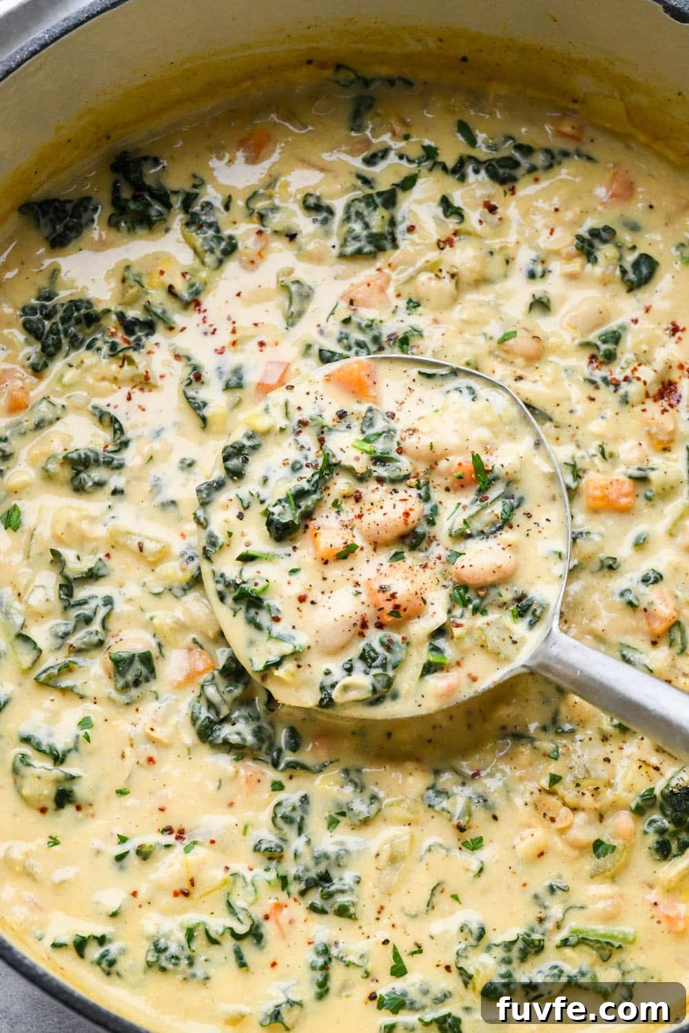 A ladle lifting out a portion of white bean and kale soup from a large pot.