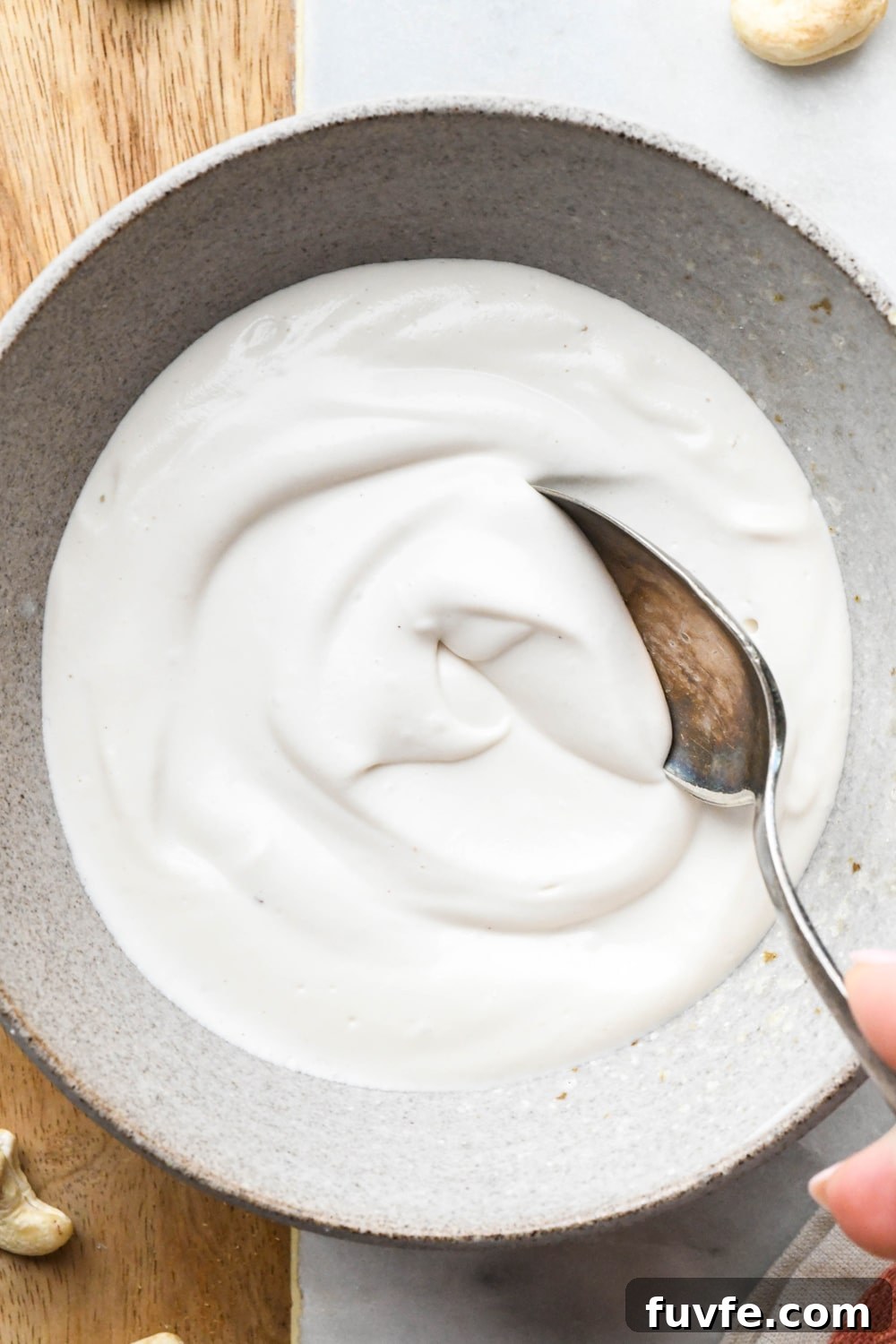 Thick and luscious cashew cream in a grey ceramic bowl, with a spoon dipping into the mixture to show the creamy texture.