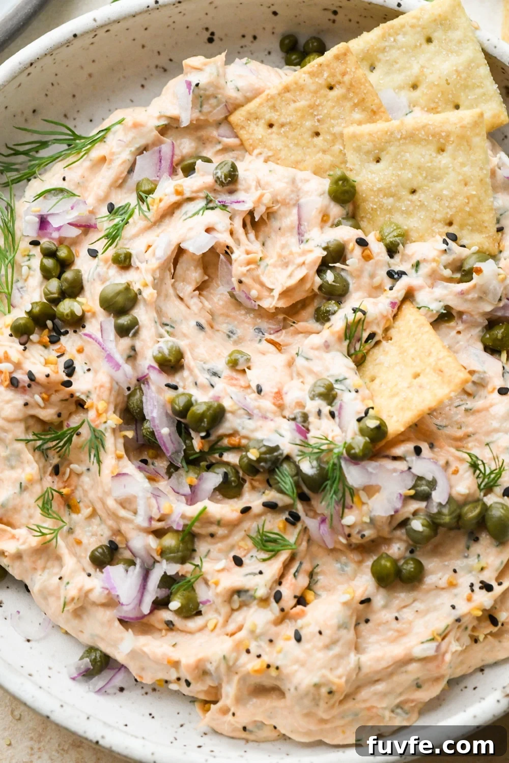 Dairy free smoked salmon dip in a shallow bowl topped with garnishes, after a cracker has scooped some of the dip out of the bowl.