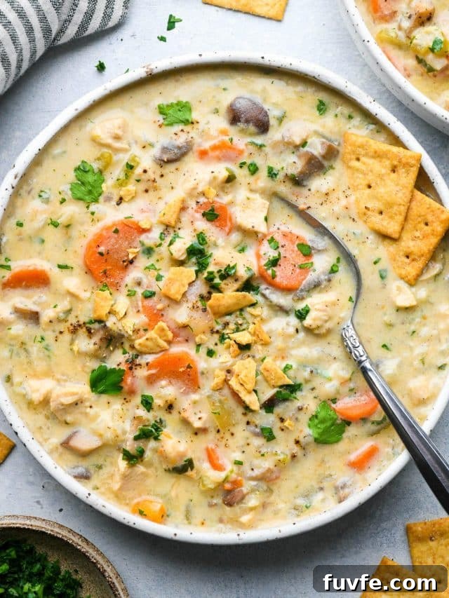 A wide shallow speckled bowl of creamy dairy free chicken and cauliflower rice soup, topped with fresh herbs and gluten free crackers.
