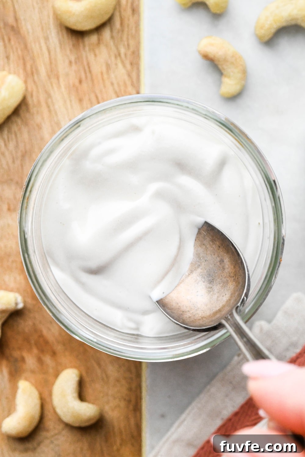 Blended cashew cream in a glass jar from the overhead perspective, with a spoon dipping into the jar to show the thick and creamy texture.