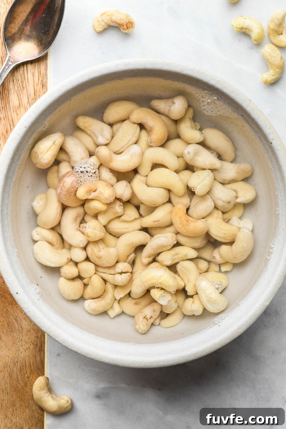 How to make cashew cream: Raw cashews in a ceramic bowl covered in hot water.