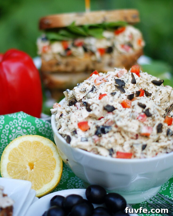A bowl of lemon chicken salad with a chicken salad sandwich in the background.
