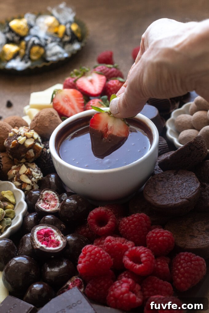 Strawberry dipped in ganache on chocolate dessert board.