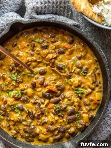 Top down view of a black cast-iron pan with a creamy light brown bean curry, on a grey background.
