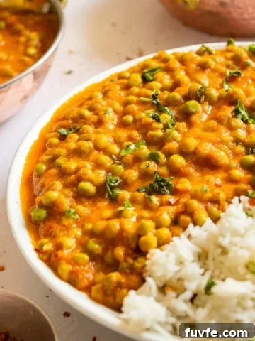 Front view of a plate with a little white rice and lots of peas in orange sauce.