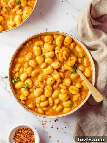 Two bowls of bean curry in sauce on white background.