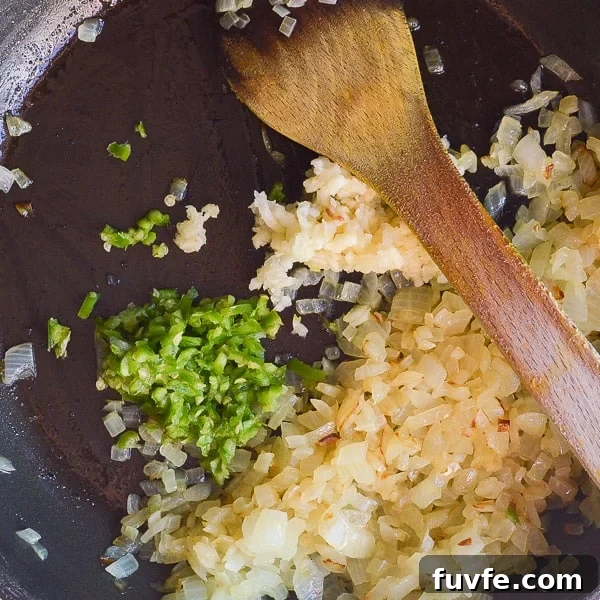 Fried onions with crushed garlic and chopped green chili in a black pan being stirred with a wooden spoon