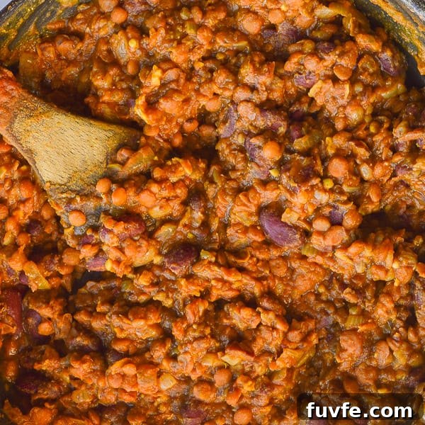 Lentils andkidney beansin a tomato and spice sauce in a pan with a wooden spoon