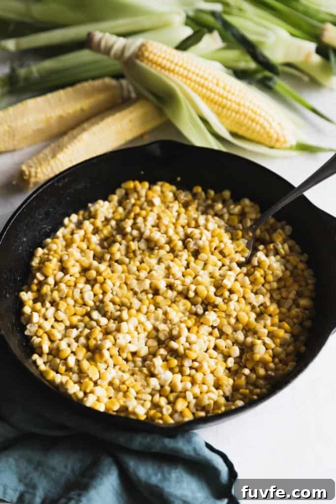 A cast iron skillet of fried corn, next to fresh ears of corn.