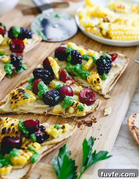 Sliced hummus flatbread with corn and berries on a wood serving board.