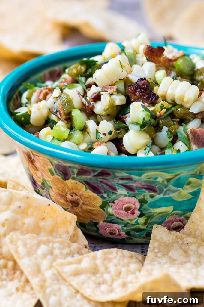 A floral bowl of corn and bacon salsa surrounded by tortilla chips.