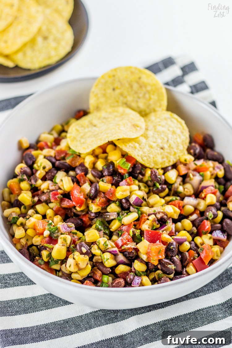A bowl of black bean and corn salsa with three tortilla chips.