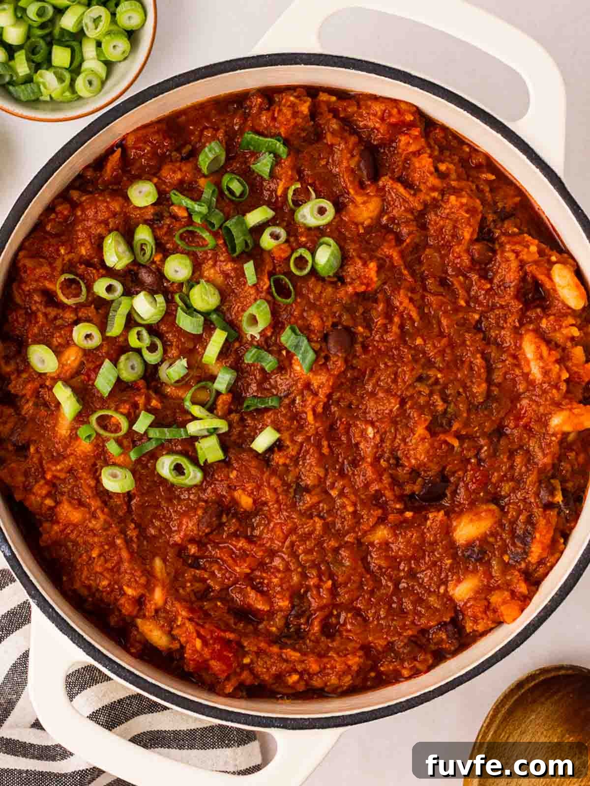 A large pot of vegan chilli on a table with spring onions on top.
