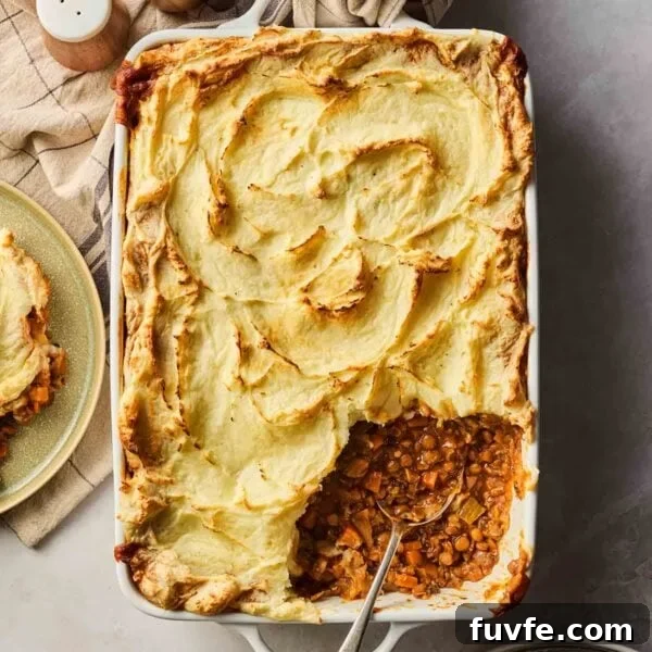 A vegetarian cottage pie straight out of the oven with a golden brown top and a portion already dished out with a spoon.