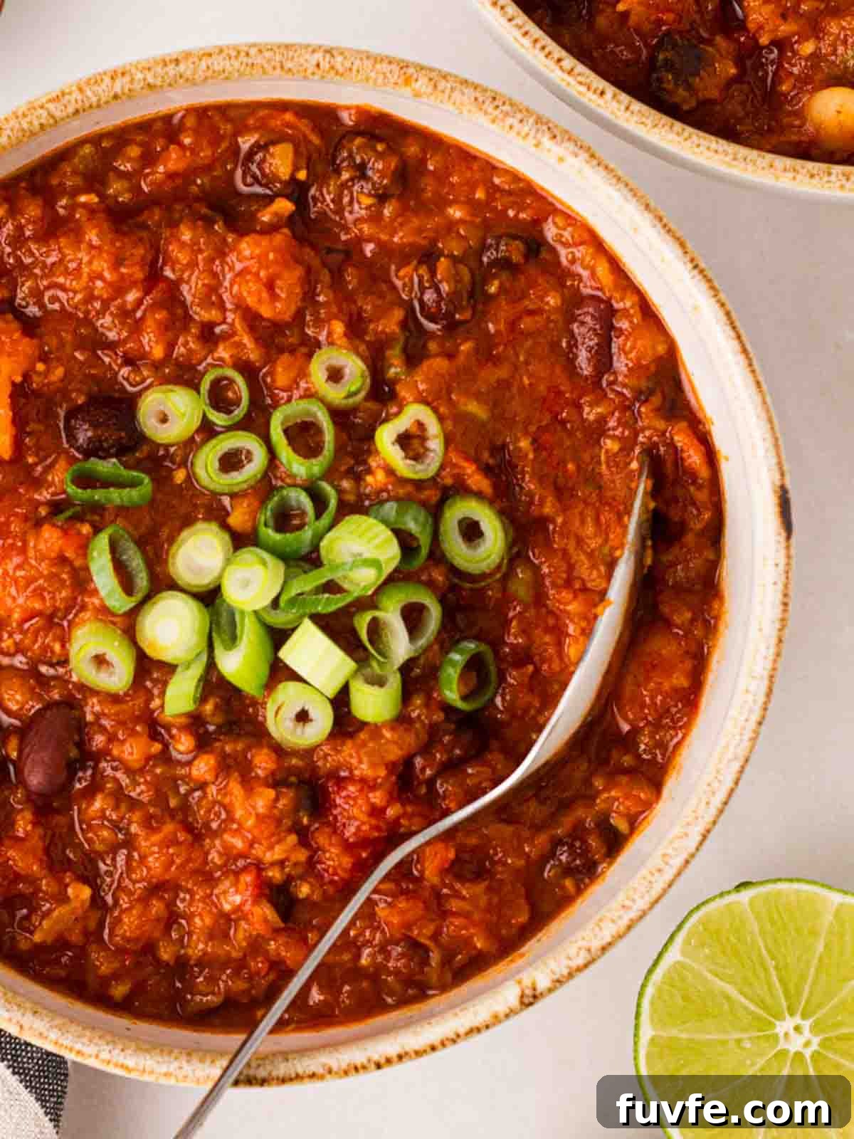 A bowl of vegan chilli with spring onions on top and a spoon to serve.