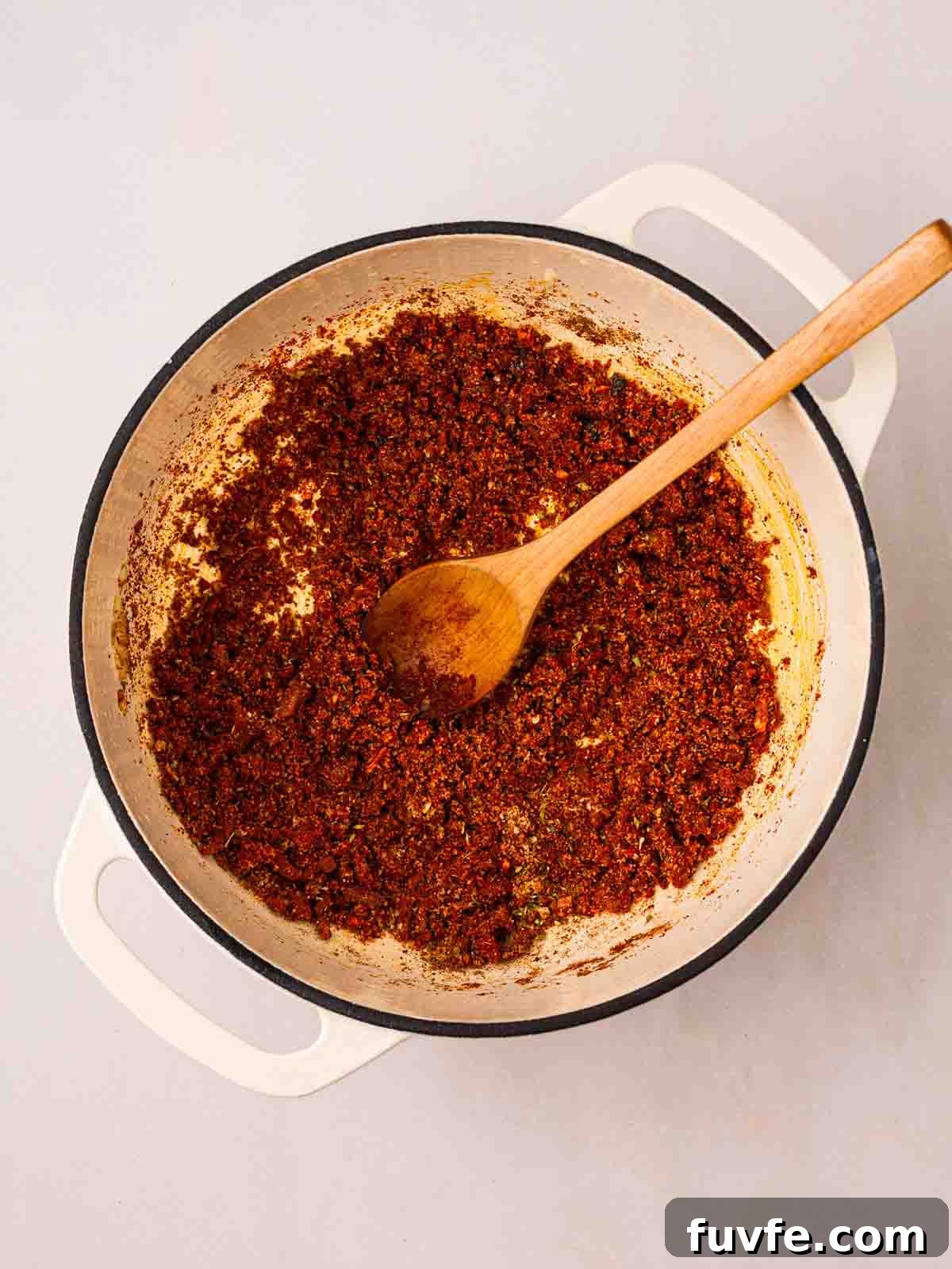 Spices cooking in a large pan with a wooden spoon.