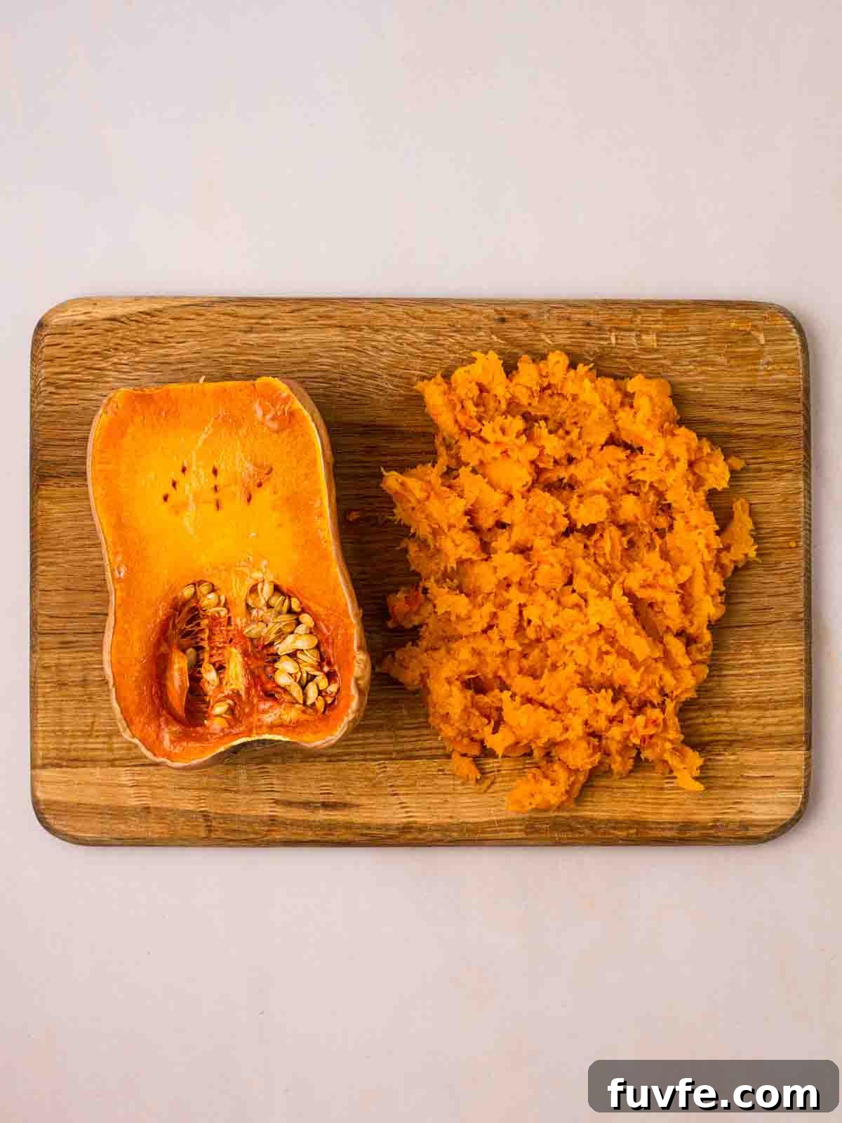 A halved butternut squash on a chopping board. One side is intact, the other half is mashed.