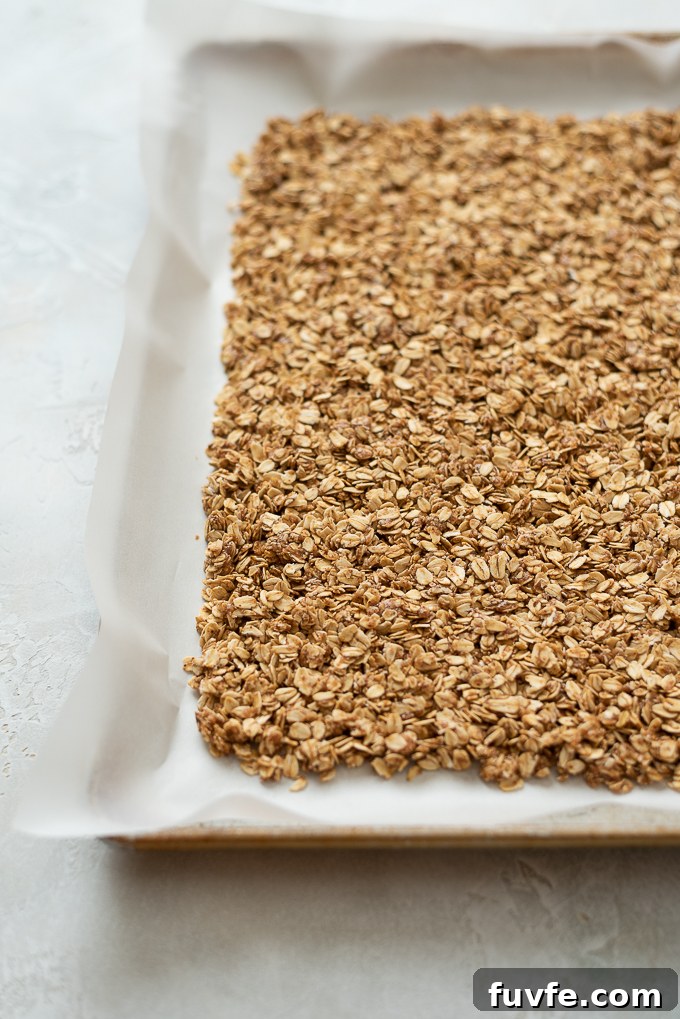 Almond butter granola packed down on a parchment lined baking sheet.