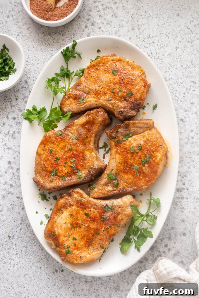 Juicy Oven-Baked Pork Chops with Garlic-Herb Crust 3 Baked bone-in pork chops on a serving platter with parsley.