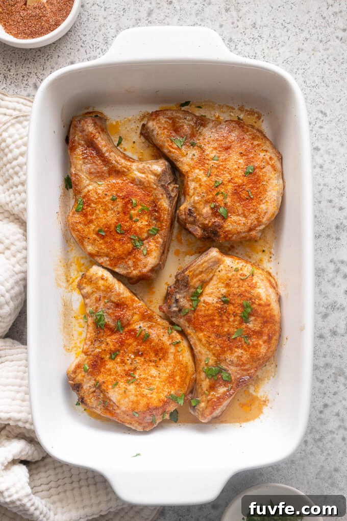 Juicy Oven-Baked Pork Chops with Garlic-Herb Crust 9 Juicy baked pork chops in baking dish with chopped parsley.