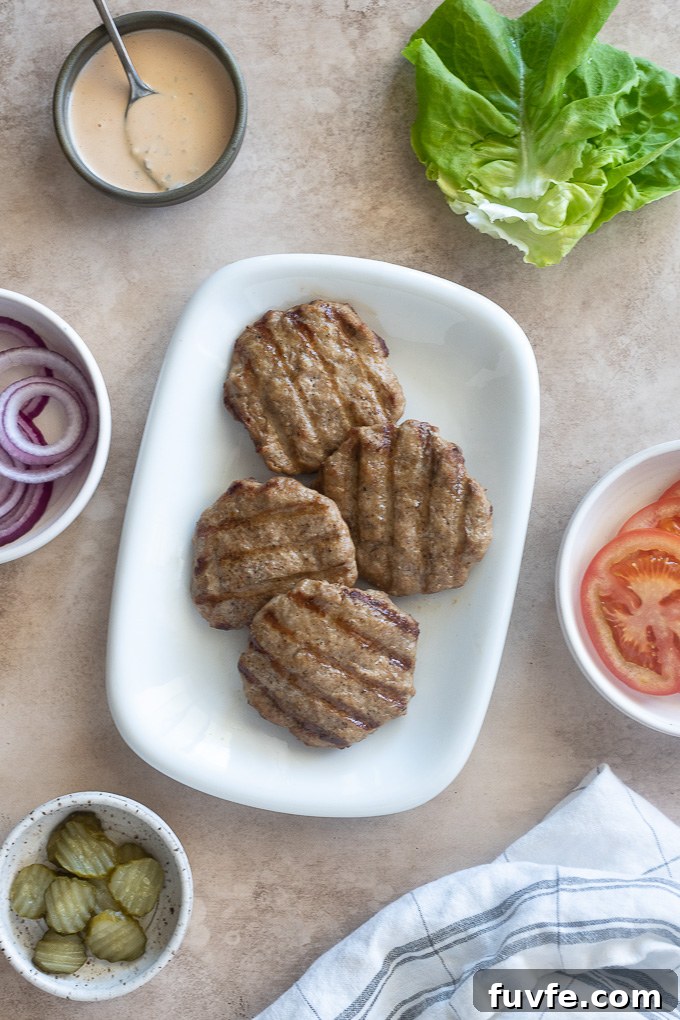 Grilled turkey burgers on a plate with condiments surrounding.