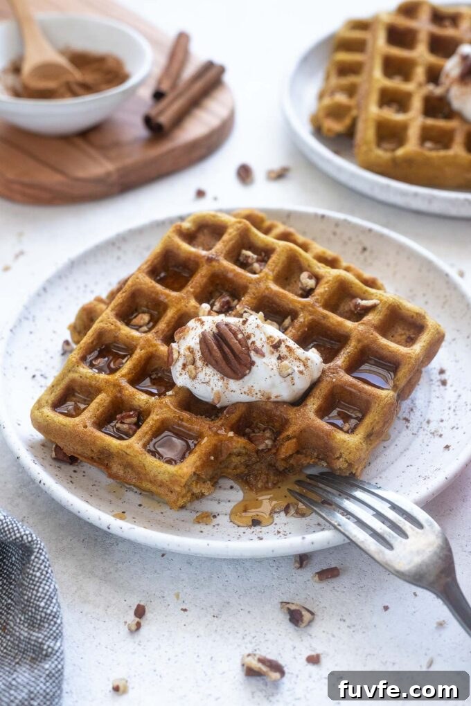 Pumpkin spice waffles on a plate with pecans and maple syrup.